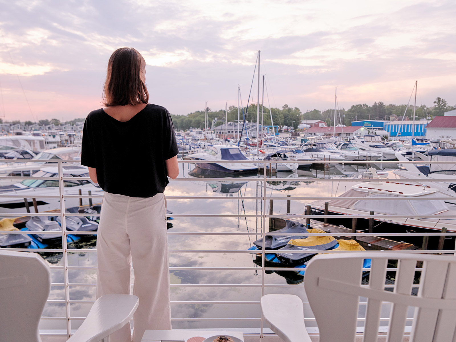 Woman looking out from balcony over pink skies and view of boats in a marina