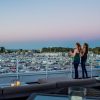Two young women enjoy cocktails on a candlelit rooftop deck at sunset, overlooking the New Buffalo Marina