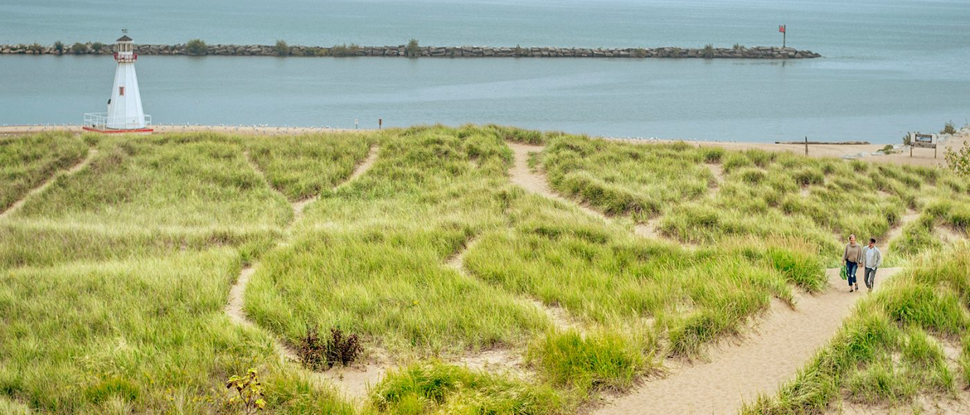 A couple walks on a sandy path amidst dune grass with Lake Michigan behind