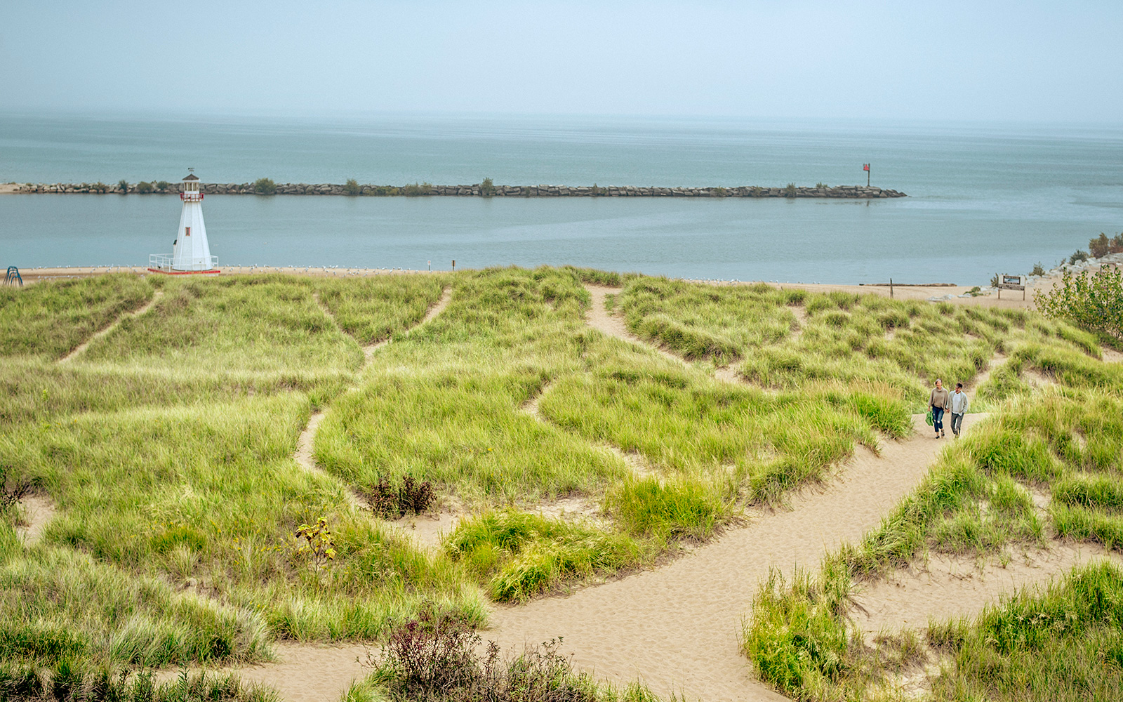  A couple walks on a sandy path amidst dune grass with Lake Michigan behind