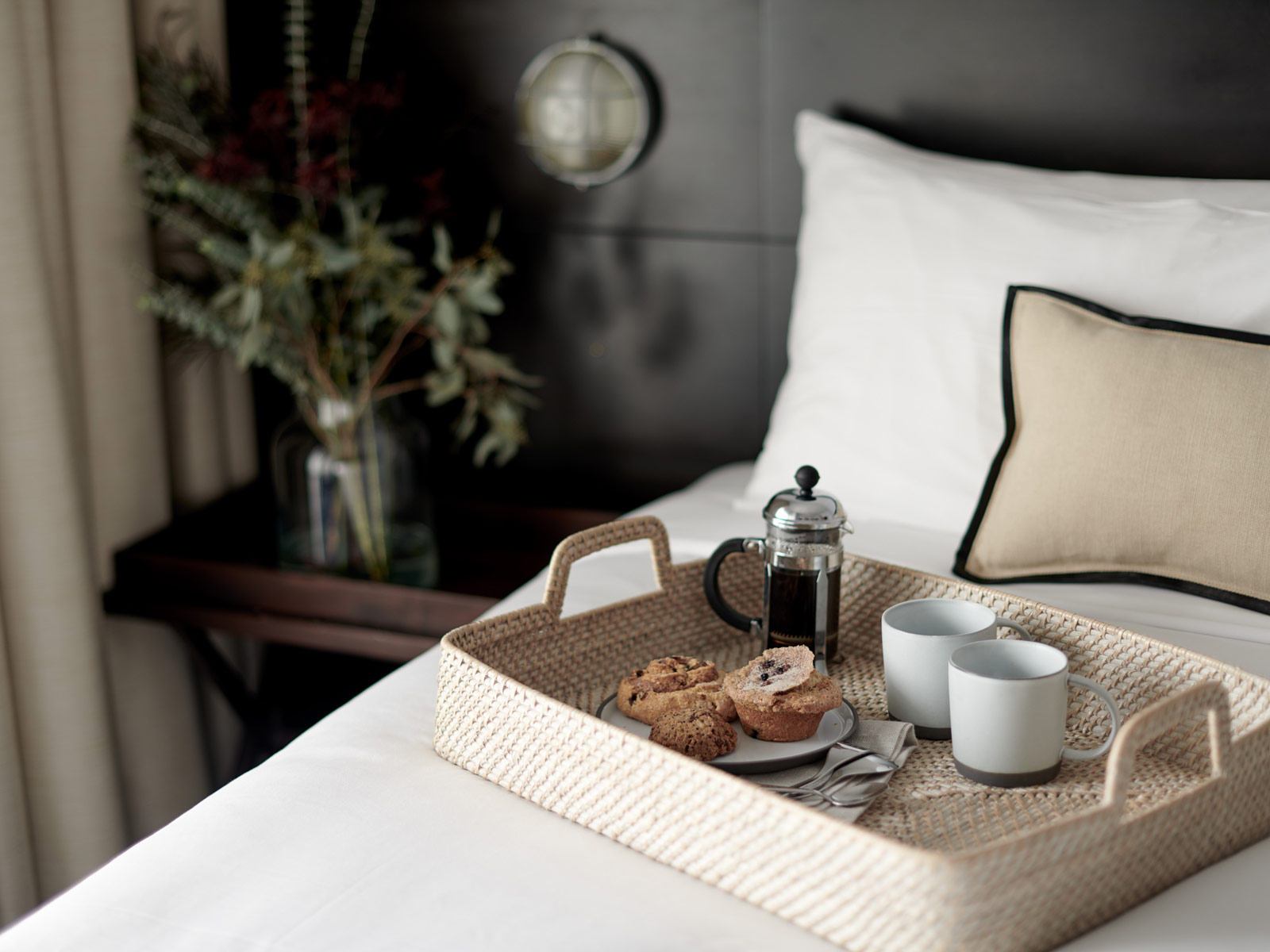 King bed with white linens and a woven basket tray with French press, two mugs and breakfast pastries at Marina Grand Resort