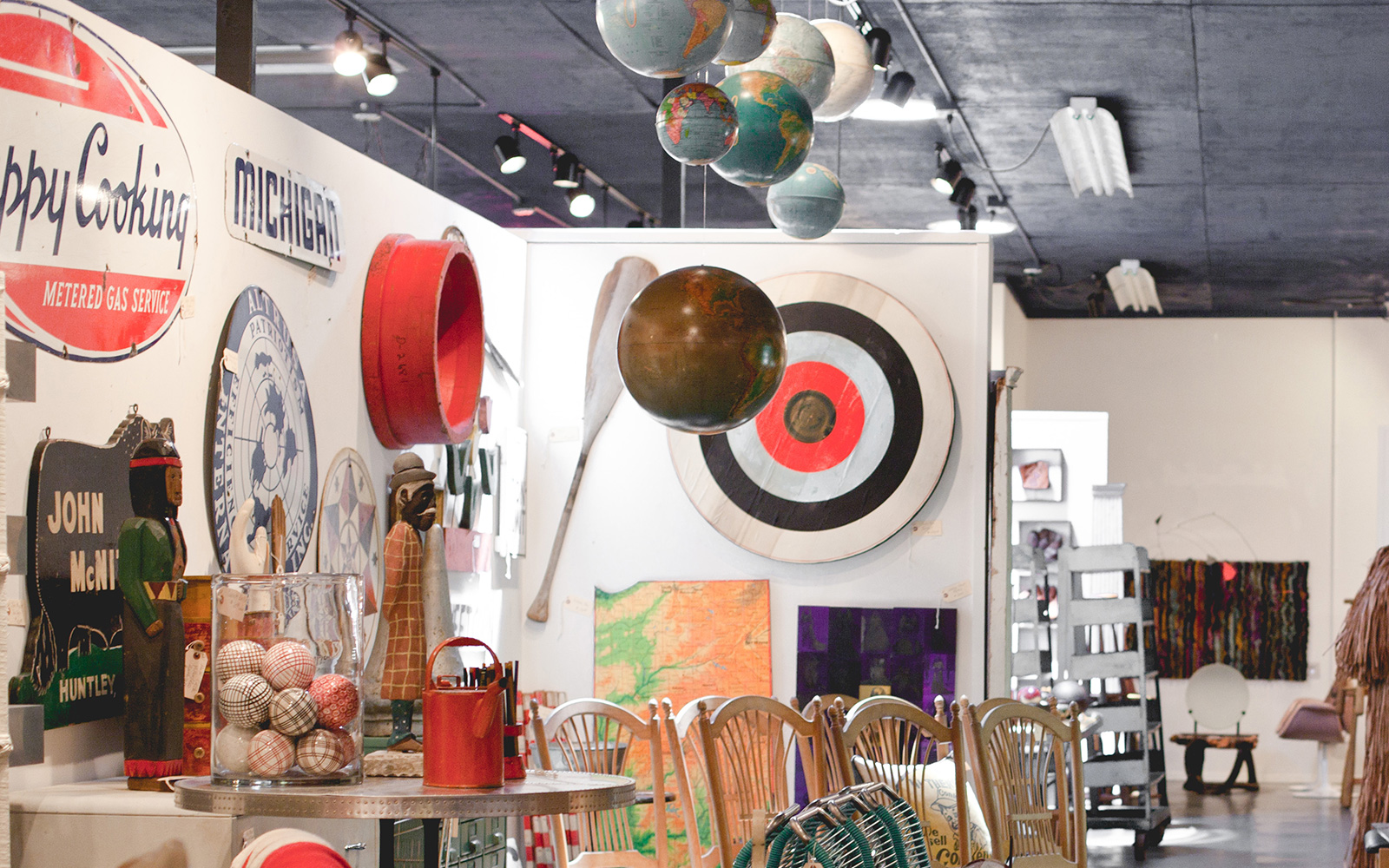 a curated antiques store with wood chairs, globes hanging from the cealing, vintage signs and more