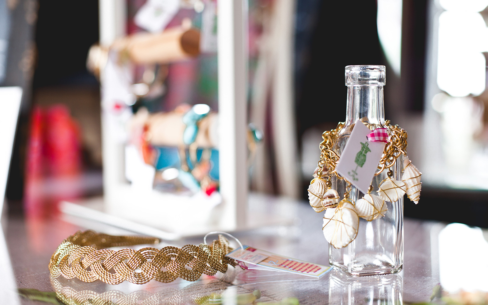 a large gold braided necklace on a table with a sea shell bracelet displayed on a glass bottle