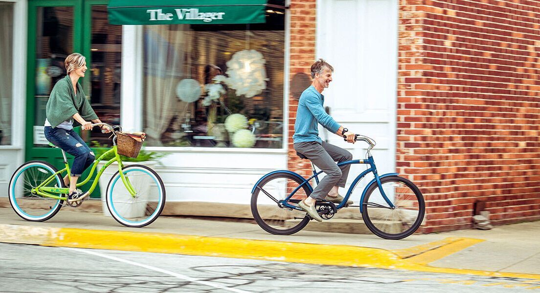a woman and a man ride cruiser bikes down a New Buffalo downtown sidewalk