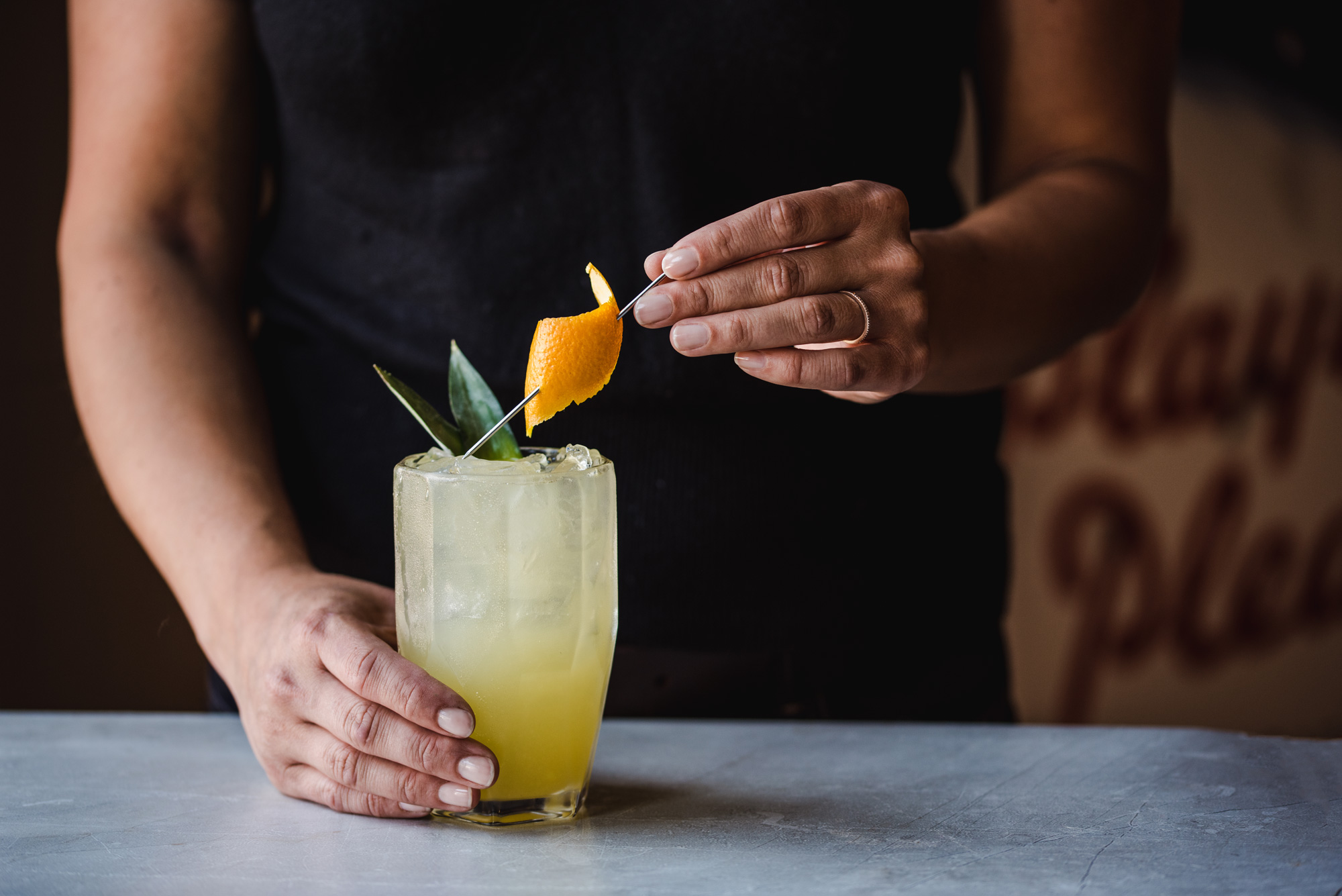 Bentwood Tavern Summer Cocktail Closeup of a bartender in a black shirt preparing a summery cocktail with pineapple juice and an orange twist garnish at Bentwood Tavern.