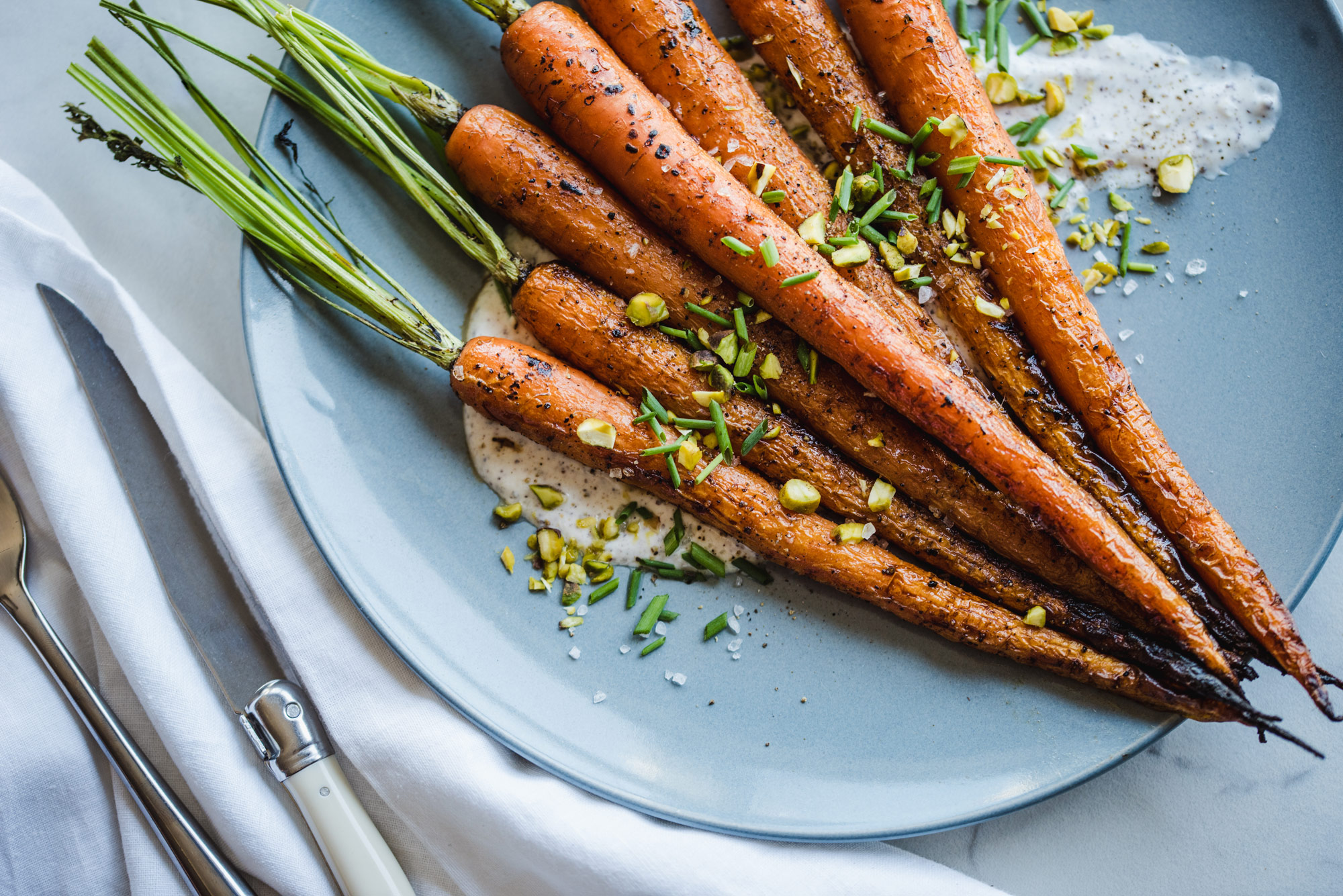 Bentwood Tavern Wood Fire Oven Roasted Carrots A light blue plate with whole roasted carrots with a sumac yogurt sauce, chives and pistachios at Bentwood Tavern.