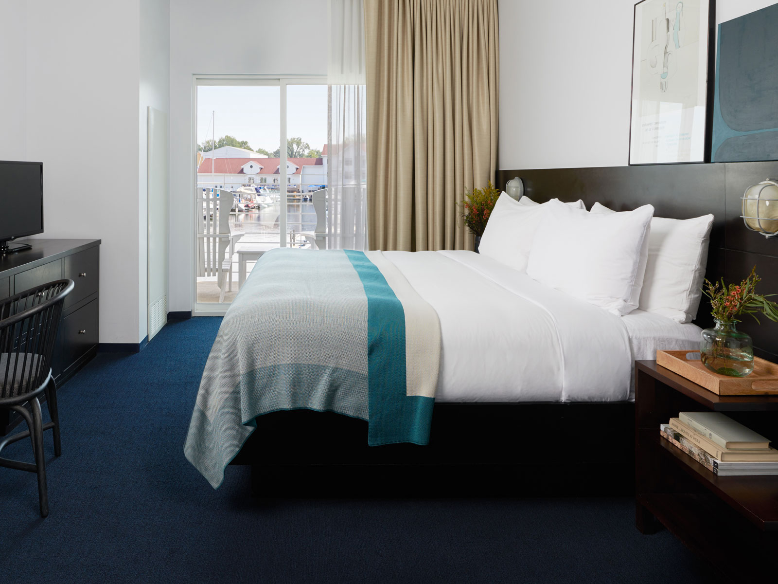 Bedroom with King Size bed, white linens, blue throw blanket and a view of the New Buffalo Marina through the window