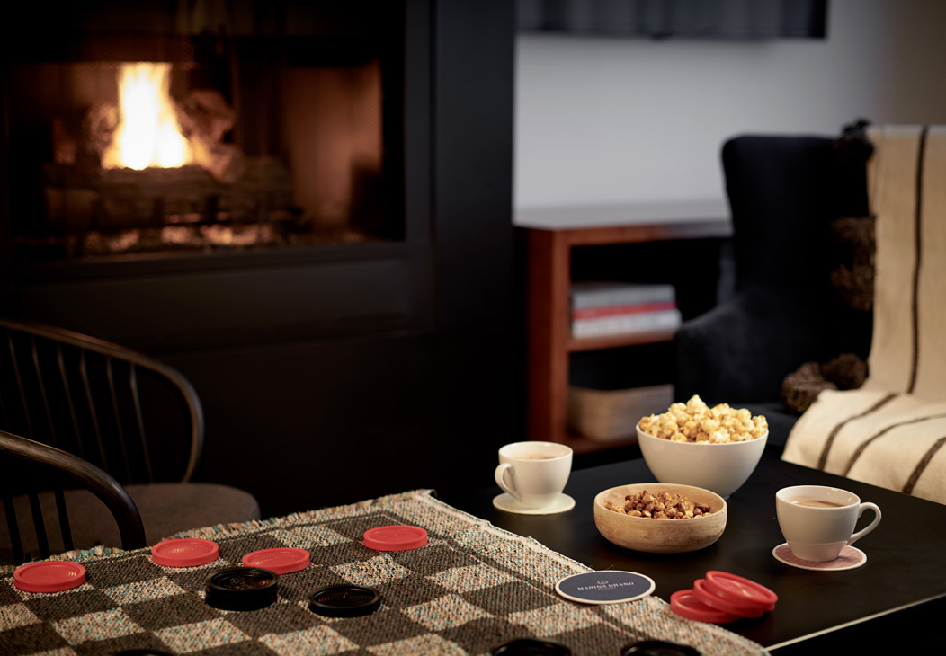 Holiday Family Fun Package Coffee table with a game of checkers, caramel corn and hot cocoa in front of a fireplace.