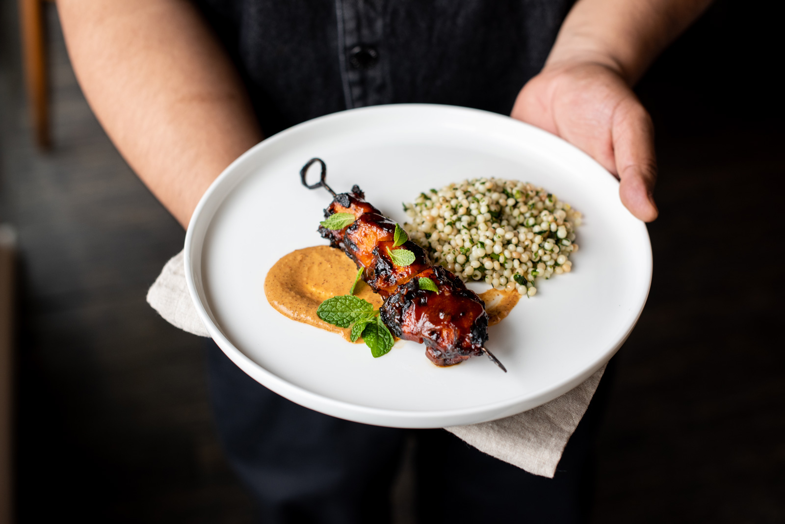 White plate with skewer of Moroccan BBQ chicken overtop couscous and garnished with fresh mint