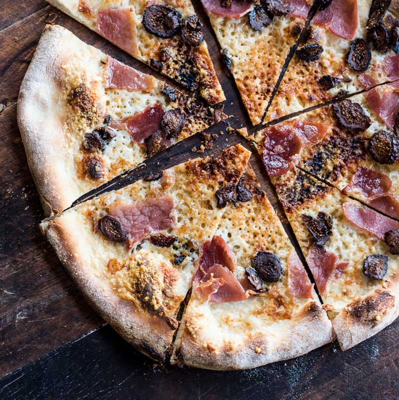 Sliced prosciutto and fig pizza on a rustic cutting board